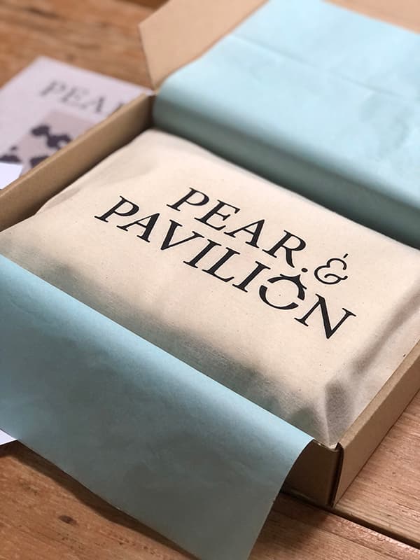 Packaged tapestry kit in bag with 'Pear & Pavilion' branding on a wooden table.