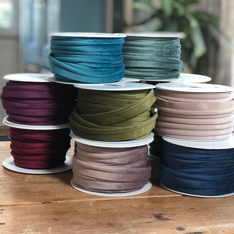 Spools of colourful velvet piping on a wood table.