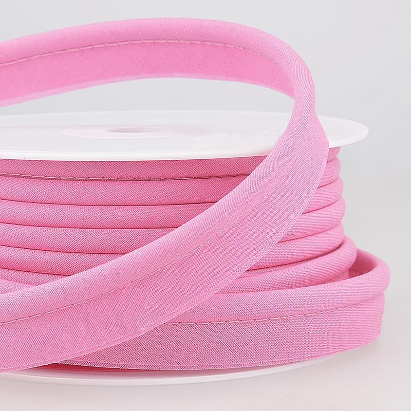 Spool of mid pink coloured piping on a white surface.