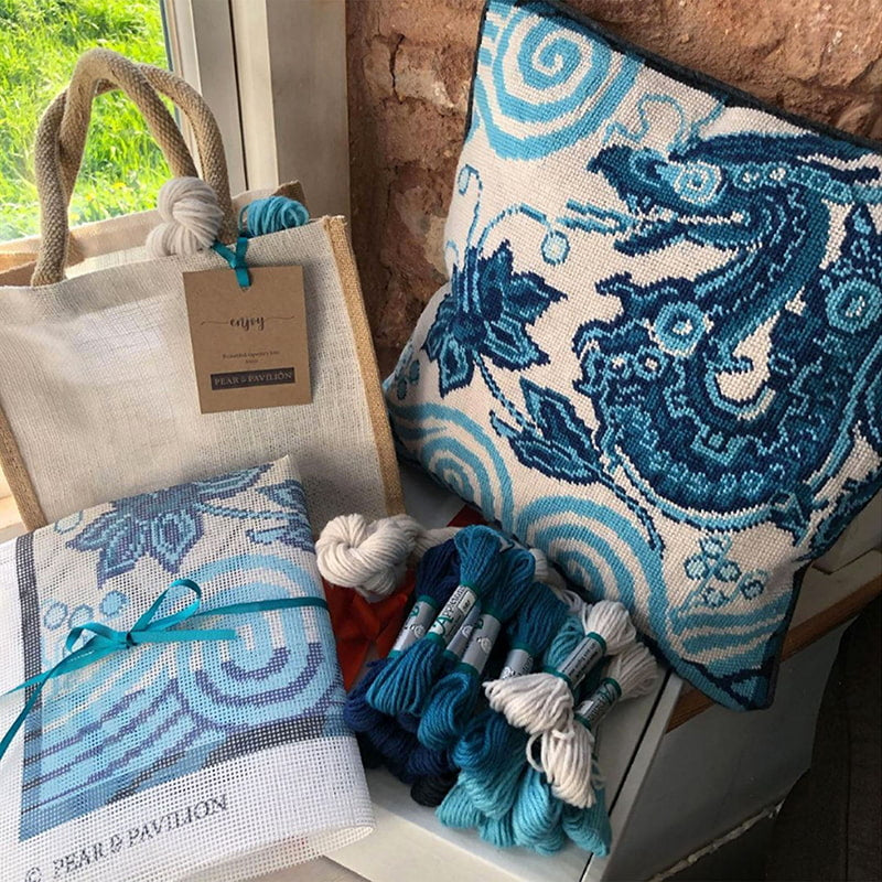 Tapestry kit contents and cushion in blue dragon design, placed on window sill against a stone wall.