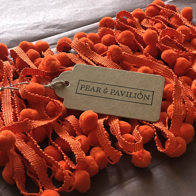 Pom pom trim in orange with packaging label.