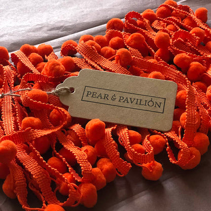 Pom pom trim in orange with packaging label.